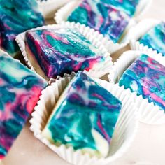 several pieces of cake sitting on top of each other in paper wrappers with blue, pink and green swirled icing