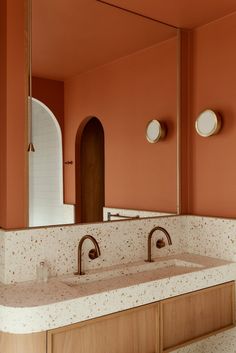 a bathroom with orange walls and two sinks in the foreground, an oval mirror on the far wall