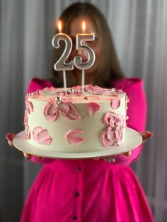 a woman holding a birthday cake with candles in the shape of twenty five on it