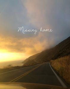 the sun is setting on an empty road near the ocean and mountains with writing that reads, missing home