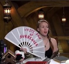 a woman holding a white fan sitting at a table