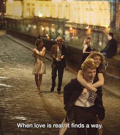 two people hugging each other while walking down the street in front of some buildings with text that reads, when love is real, it finds a way