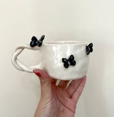 a hand holding a white coffee cup with black bow decorations on it's side