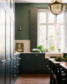 a kitchen with dark green cabinets and white tile flooring, along with a chandelier hanging from the ceiling