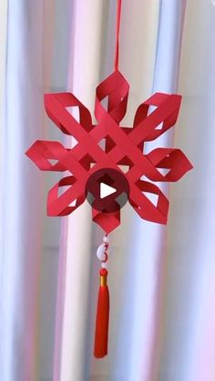 a red paper snowflake hanging from a string with a tassel on it