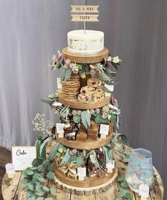 a three tiered cake sitting on top of a wooden table covered in greenery