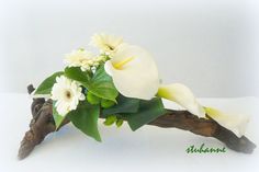 a white flower arrangement sitting on top of a wooden branch