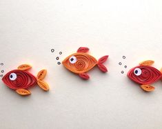 three red and orange fish with googly eyes on white paper next to each other