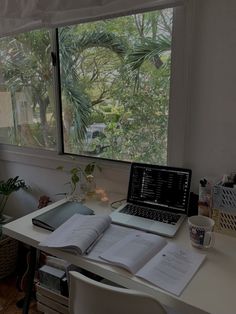 a laptop computer sitting on top of a white desk next to a book and cup