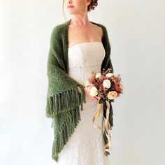 a woman in a white dress holding a bouquet and wearing a green shawl over her shoulder