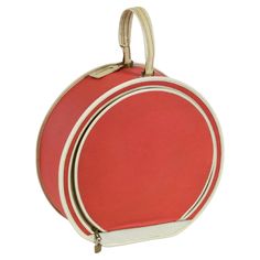 a red and white round purse with two handles on the front, hanging from a metal hook