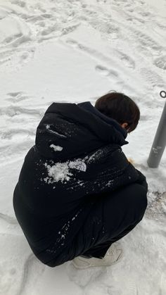 a person kneeling down in the snow next to a pole