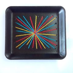 a black square plate with colored sticks in the shape of a sunburst on it