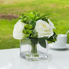 a vase filled with white flowers sitting on top of a table next to a cup