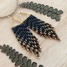 a pair of black and gold earrings on a wooden table next to green leafy plants