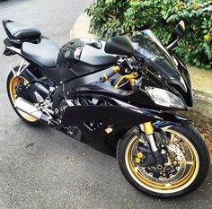 a black and gold motorcycle parked on the side of the road next to some bushes