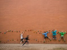 four people climbing up the side of a brick wall with their hands in the air