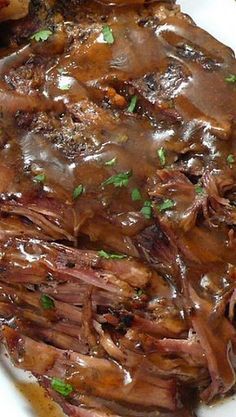 a white plate topped with roast beef covered in gravy and garnished with parsley