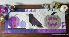 the table is covered with purple and white quilts, coffee cups, and other items