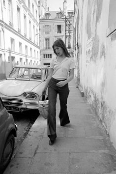 a woman walking down a street next to parked cars