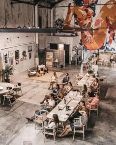 people are sitting at tables in an industrial building with paintings on the walls and floor