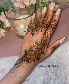 a woman's hand with henna tattoos on it and flowers in the background