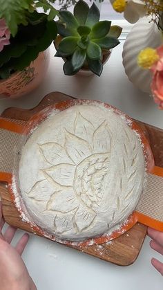 a person is making a cake on a wooden cutting board with flowers in the background