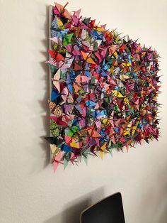 an art piece made out of colorful origami pieces on a white wall next to a black chair