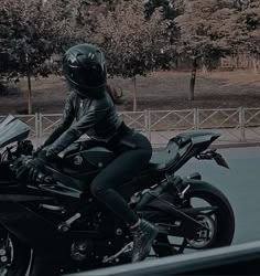 a person riding on the back of a black motorcycle down a street with trees in the background