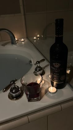 a bottle of wine sitting on top of a bath tub next to a glass filled with liquid