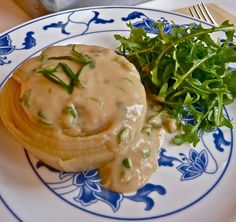 a blue and white plate topped with food next to a green leafy salad on top of a wooden table