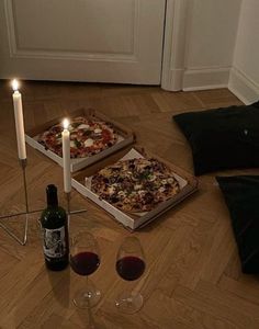 two pizzas and wine on the floor in front of a white door with candles