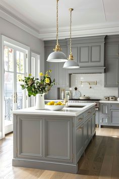 a kitchen with gray cabinets and white counter tops, yellow flowers in a vase on the island