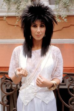 a woman with black hair standing in front of a gate wearing a white shirt and skirt