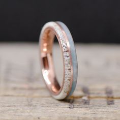 a close up of a wedding ring on top of a piece of wood with white and pink gold inlays