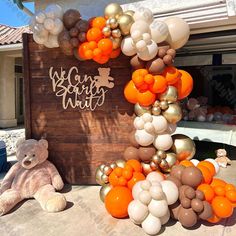 an orange and white balloon arch in front of a house with a teddy bear laying on the ground