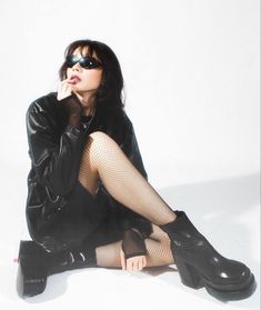 a woman in fishnet stockings and boots sitting on the ground with her hand under her chin