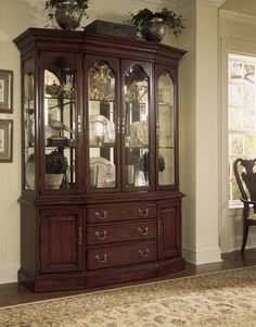 a large wooden china cabinet with glass doors and drawers in a living room area next to a dining room table