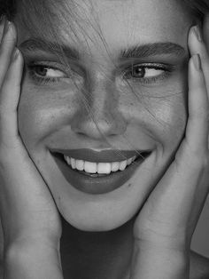 a black and white photo of a smiling woman with her hands on her face,