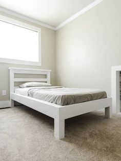 a white bed sitting in the middle of a bedroom next to a window with no curtains