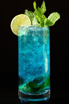 a tall glass filled with blue liquid and lime