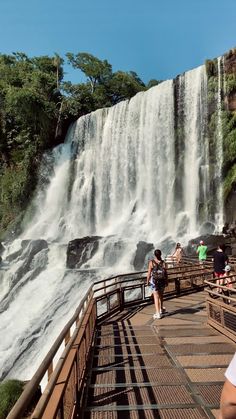 people are standing at the edge of a bridge near a waterfall with water cascading over it