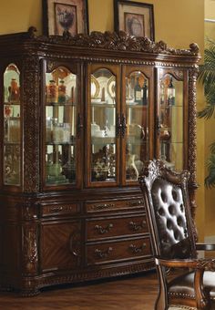 an ornate wooden china cabinet with glass doors and carvings on the front, in a living room