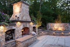 an outdoor fireplace surrounded by stone walls and benches with lights on each side that illuminates the fire