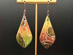 a pair of earrings hanging from a hook on a stand in front of a black background