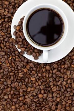 a cup of coffee sitting on top of a pile of coffee beans