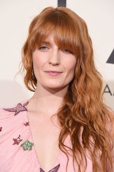 a woman with red hair wearing a pink dress and smiling at the camera while standing in front of an awards room