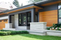 a modern house with wood siding and stone planters on the front porch, along with grass