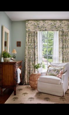 a living room filled with furniture and windows covered in floral curtained drapes next to a dresser