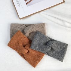 three knitted scarves are laying next to each other on a white sheet with an open book in the background